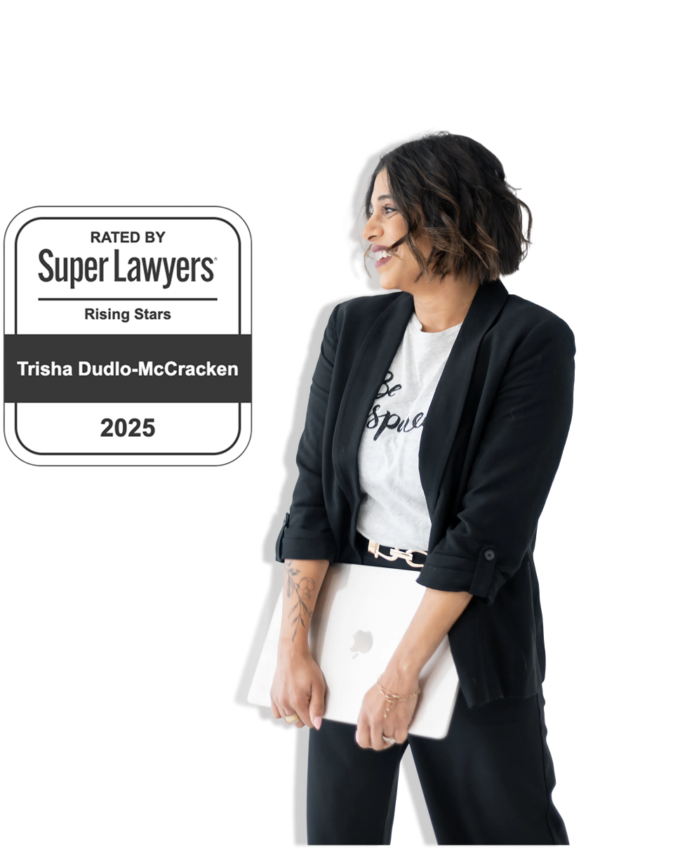 A woman in a black blazer and white t-shirt holds a closed laptop and smiles. Next to her is a “Super Lawyers Rising Stars 2025” badge with the name Trisha Dudlo-McCracken. The background is plain white.